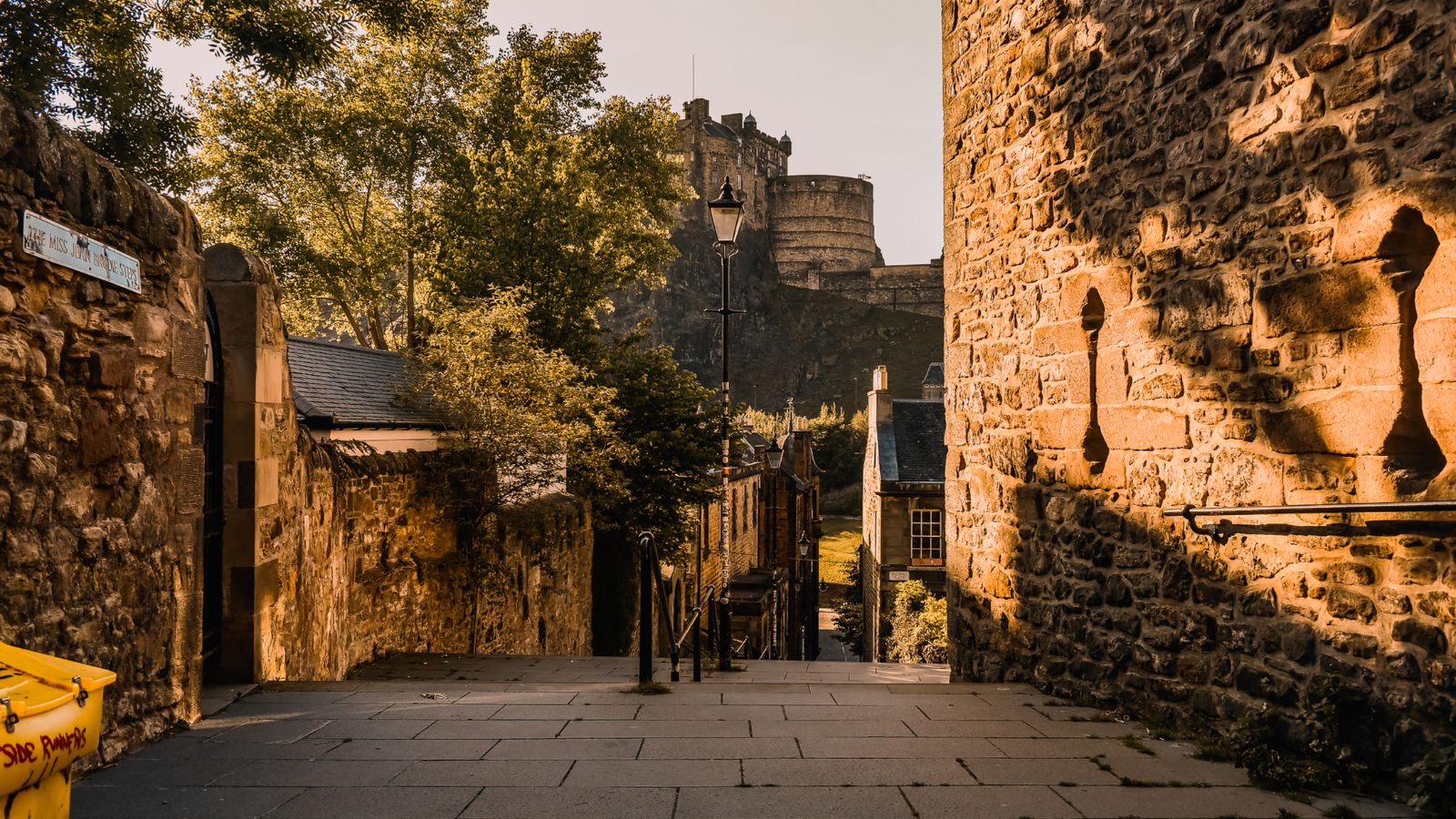 A street in Edinburgh with old stone walls and a view of the Edinburgh Castle.